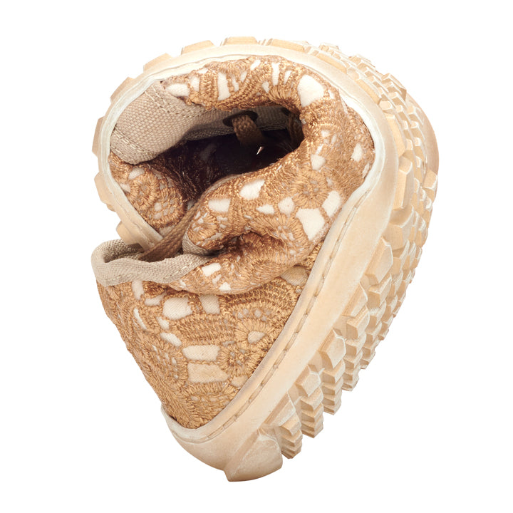 QELLY Beige Gold-sneakern från ZAQQ med en ljusbrun och beige virkdesign och en tjock, robust sula är böjd i mitten för att demonstrera sin rörelsefrihet. Barfotaskon står på en vit bakgrund.