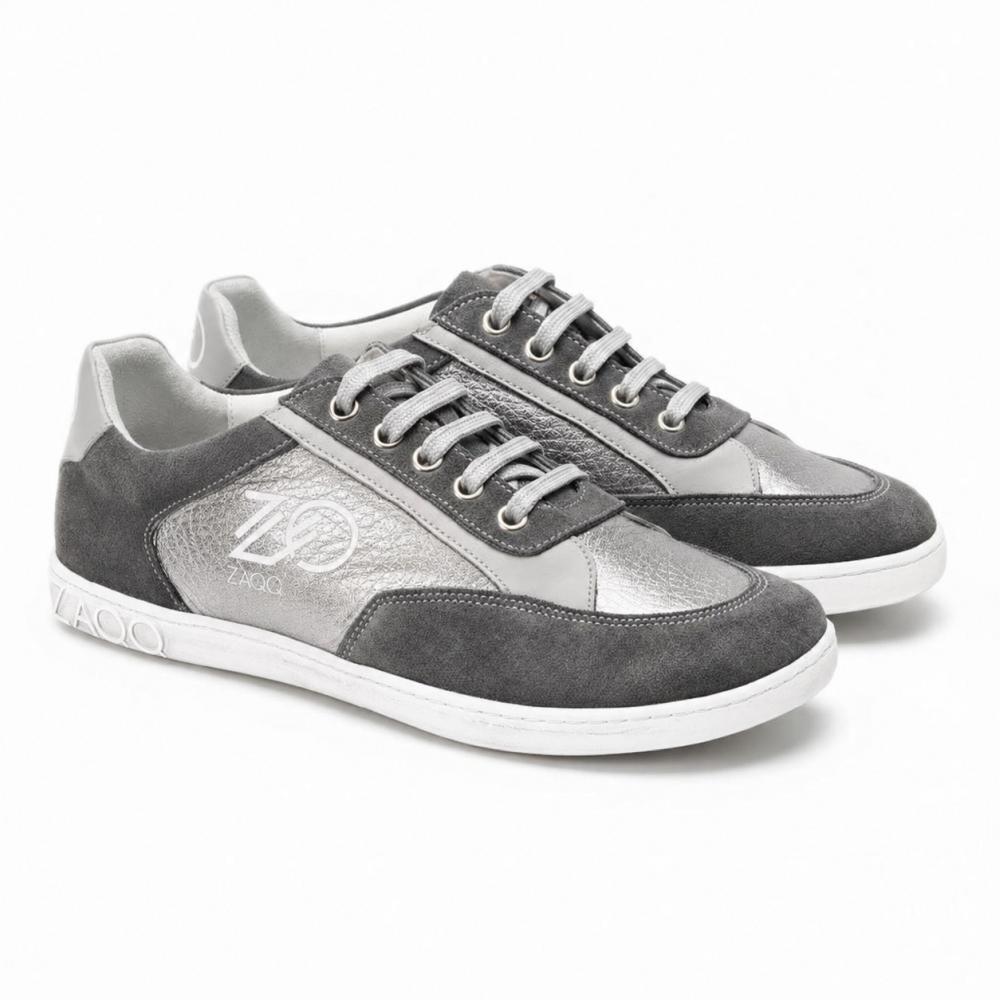 Ett par OQTAV Grey-sneakers från ZAQQ, tillverkade av sammetslen mocka och strukturerade insatser. Med silvriga skosnören och den distinkta Zagoo-logotypen på sidan och hälen presenteras dessa stiliga skor sida vid sida på en vit bakgrund.