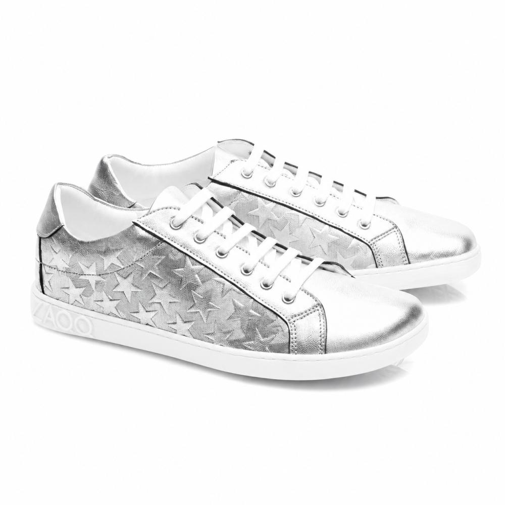 SLOQ Stars Silver-sneaker från ZAQQ har vita skosnören och stjärnmönster på sidorna, kompletterat med en vit sula med VAOO-prägling på hälen. Dessa skor kännetecknas av en slank och modern design med en glänsande metallic-finish.