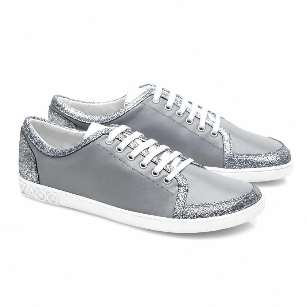 TIQQ Grey Silver Sneaker från ZAQQ imponerar med sin enkla design av mjukt nappaläder med vita skosnören och silverglitterdetaljer, kompletterat med vita sulor och en diskret logotyp på hälen, och erbjuder den perfekta blandningen av stil och komfort för varje tillfälle.