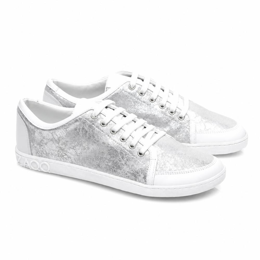 Vi presenterar TIQQ Silver White från ZAQQ: Ett par stiliga sneakers i högkvalitativt nappaläder med en iögonfallande metallisk-silver textur och vita sulor. Dessa sneakers är utrustade med strålande vita skosnören, dekorativa sömmar och en distinkt 4000-detalj på sidan av sulan.